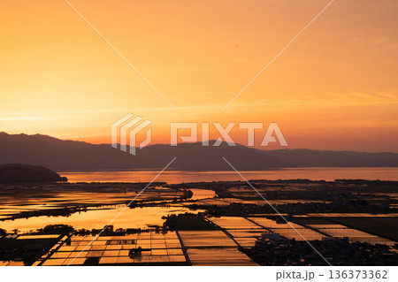 滋賀県東近江市猪子町の猪子山から望む水張りの田植え前の水田がオレンジ色に光る夕景 136373362
