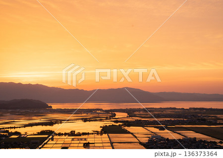 滋賀県東近江市猪子町の猪子山から望む水張りの田植え前の水田がオレンジ色に光る夕景 136373364