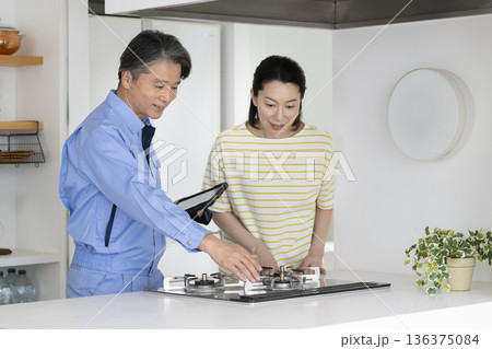 ガスコンロを点検する業者と話を聞くミドルの女性 ガスコンロを点検する業者と話を聞くミドルの女性 136375084