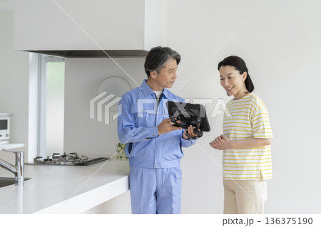 タブレットを見せて説明をする業者と話を聞くミドルの女性 タブレットを見せて説明をする業者と話を聞くミドルの女性 136375190