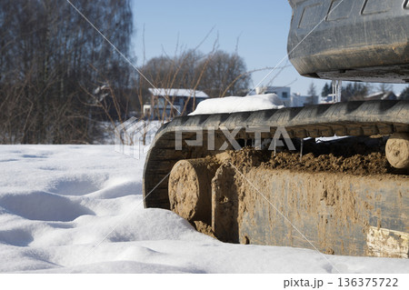 Close-up of excavator tracks covered in mud and snow on a construction site 136375722