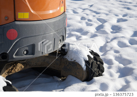 Close-up of an excavator's track and orange body in the snow 136375723