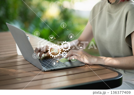 Woman using laptop with CO2 emission reduction and green energy icons. Concept of sustainability, net zero emissions, environmental conservation, and renewable technology for climate change. 136377409
