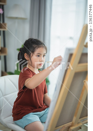 Young Girl Painting on Canvas in Bright and Cozy Room, Exploring Creativity and Artistic Skills with Brush in Hand 136377446