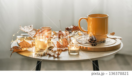 Cozy composition with a cup, candles and autumn leaves in the interior. Cozy composition with a cup, candles and autumn leaves in the interior. 136378821