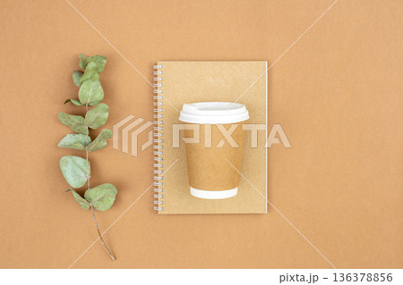 Craft paper coffee cup, notebook and eucalyptus sprig on eco background, flat lay. 136378856