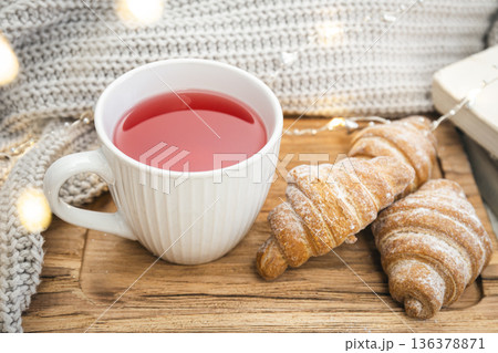 A cup of red tea, a croissant and a knitted element on a wooden tray. A cup of red tea, a croissant and a knitted element on a wooden tray. 136378871