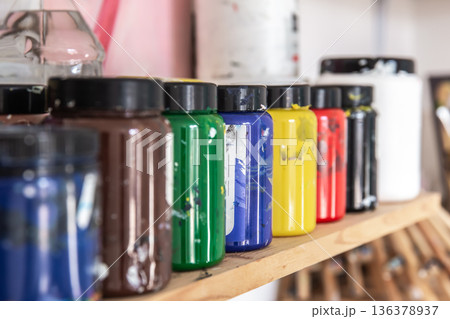 Colored paints for drawing and painting in cans on a shelf in a workshop. Colored paints for drawing and painting in cans on a shelf in a workshop. 136378937