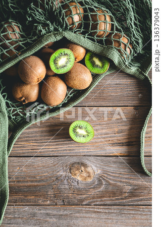 Fruits of kiwi in a mesh bag on a wooden background, top view, rustic style, 136379043