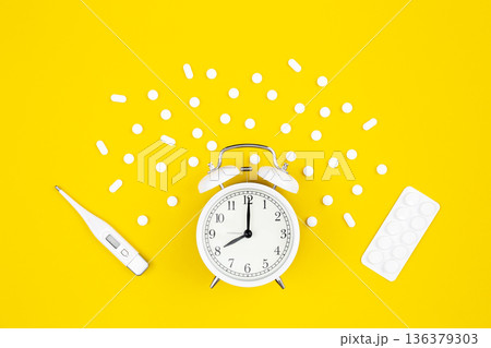 Alarm clock, medical thermometer and pills on a yellow background, flat lay. 136379303