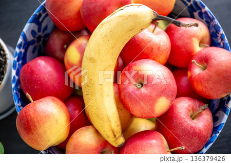 Banana and ripe red apples in a bowl in the kitchen. 136379426