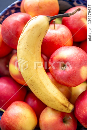 Banana and ripe red apples in a bowl in the kitchen. 136379427