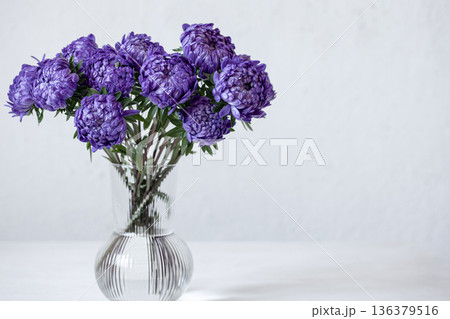 Glass vase with a bouquet of blue chrysanthemums on light background. 136379516