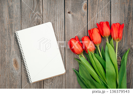 Bouquet of red tulips and notebook on a wooden background, top view. Bouquet of red tulips and notebook on a wooden background, top view. 136379543