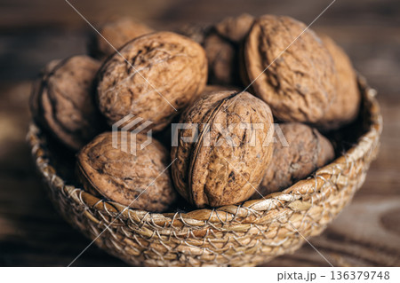 Close-up, whole walnuts in a wicker bowl on a wooden background. 136379748