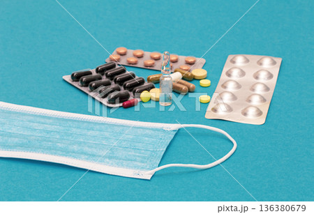 A variety of pills and a protective face mask on a blue background. A variety of pills and a protective face mask on a blue background. 136380679