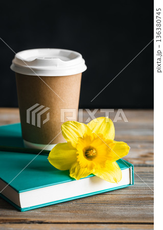 Paper cup, book and yellow flower on a blurred wooden background. Paper cup, book and yellow flower on a blurred wooden background. 136380745
