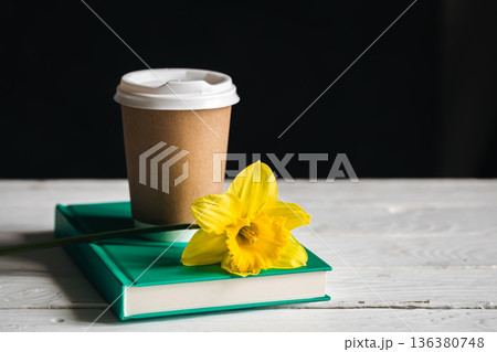 Paper cup, book and yellow flower on a blurred wooden background. Paper cup, book and yellow flower on a blurred wooden background. 136380748