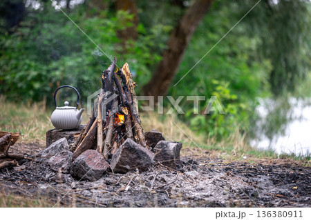 Small kettle is heated on a bonfire, outdoor recreation concept. Small kettle is heated on a bonfire, outdoor recreation concept. 136380911