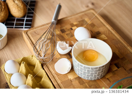 Cracked egg in bowl with whisk and eggs on wooden cutting board Cracked egg in bowl with whisk and eggs on wooden cutting board 136381434