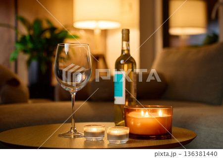 Bottle of white wine, wine glass and candles on table in living room 136381440