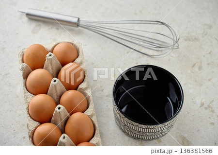 Brown chicken eggs in carton with whisk and bowl on kitchen table Brown chicken eggs in carton with whisk and bowl on kitchen table 136381566