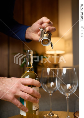 Hand removing cork from white wine bottle with corkscrew 136381570
