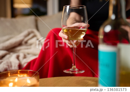 Woman holding glass of white wine during cozy evening at home 136381573