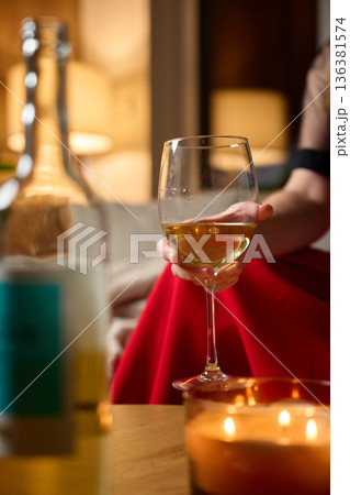 Woman holding glass of white wine during cozy evening at home Woman holding glass of white wine during cozy evening at home 136381574