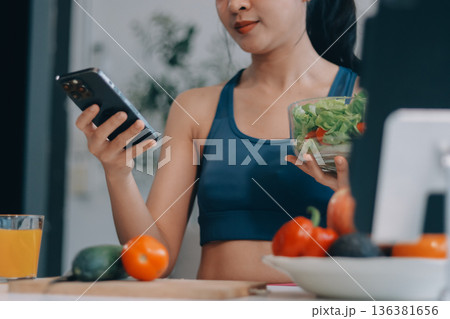 Fit young Asian women in activewear sitting on yoga mat and eating fresh vegetable salad after workout, representing clean eating, fitness lifestyle, wellness routine and health balance. Fit young Asian women in activewear sitting on yoga mat and eating fresh vegetable salad after workout, representing clean eating, fitness lifestyle, wellness routine and health balance. 136381656