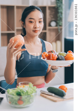 Fit young Asian women in activewear sitting on yoga mat and eating fresh vegetable salad after workout, representing clean eating, fitness lifestyle, wellness routine and health balance. Fit young Asian women in activewear sitting on yoga mat and eating fresh vegetable salad after workout, representing clean eating, fitness lifestyle, wellness routine and health balance. 136381661