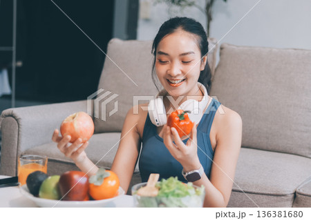Fit young Asian women in activewear sitting on yoga mat and eating fresh vegetable salad after workout, representing clean eating, fitness lifestyle, wellness routine and health balance. 136381680