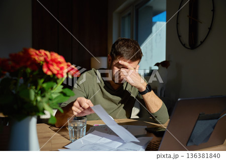 Stressed man reviewing household bills and financial documents at home Stressed man reviewing household bills and financial documents at home 136381840