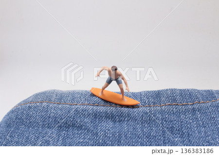 Miniature surfer rides imaginary wave formed by denim Miniature surfer rides imaginary wave formed by denim 136383186