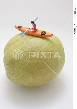 Miniature kayaker paddles orange boat atop giant pear Miniature kayaker paddles orange boat atop giant pear 136383220