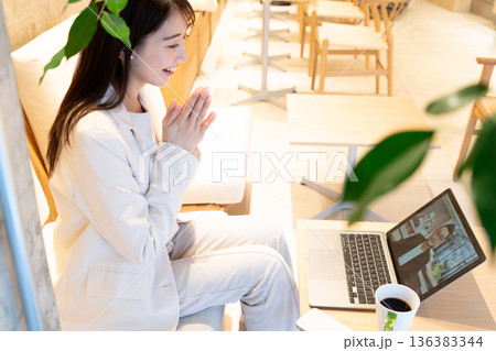 カフェのソファー席に座りパソコンでリモート会議をしている若い女性 136383344