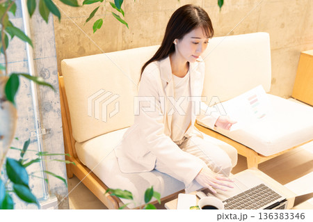 カフェのソファー席に座りパソコンでリモート会議をしている若い女性 136383346