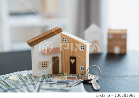 Wooden model houses on a table with fanned out dollar bills and keys, representing home ownership and real estate investment concepts Wooden model houses on a table with fanned out dollar bills and keys, representing home ownership and real estate investment concepts 136383963