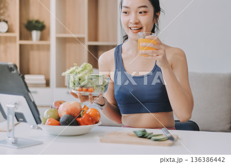 Fit young Asian women in activewear sitting on yoga mat and eating fresh vegetable salad after workout, representing clean eating, fitness lifestyle, wellness routine and health balance. 136386442