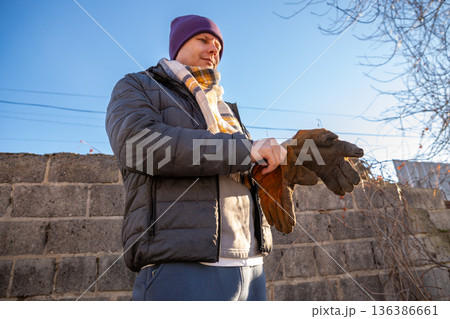 man wears brown leather welding gloves of cowhide leather to handle hot metal. protection against hand burns during welding with an electrode or gas. Farm worker, builder, groom, general laborer man wears brown leather welding gloves of cowhide leather to handle hot metal. protection against hand burns during welding with an electrode or gas. Farm worker, builder, groom, general laborer 136386661