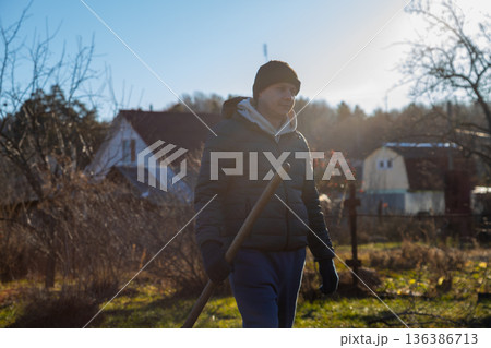 Caucasian man farm worker or gardener walks with shovel through garden. Farmer concept for organic gardening and agriculture in spring or autumn. 136386713