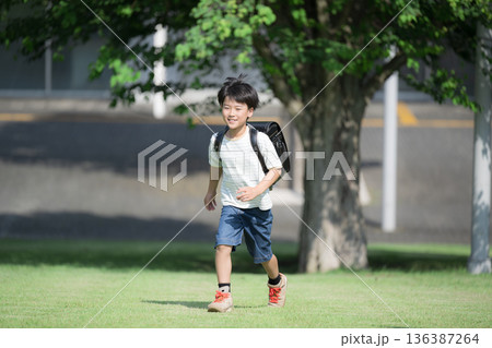 学校の校舎を背景に校庭でランドセルを背負って走る少年の(男の子)男子 学校の校舎を背景に校庭でランドセルを背負って走る少年の(男の子)男子 136387264