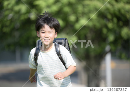 学校の校舎を背景に校庭でランドセルを背負って走る少年の(男の子)男子の笑顔のクローズアップ 136387287