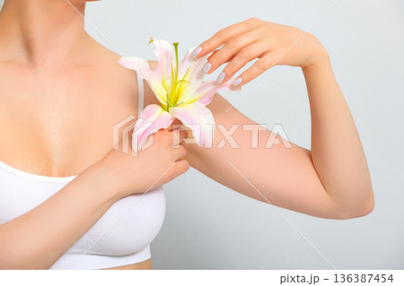 Woman with lily flower on grey background, closeup. Skin care concept Woman with lily flower on grey background, closeup. Skin care concept 136387454
