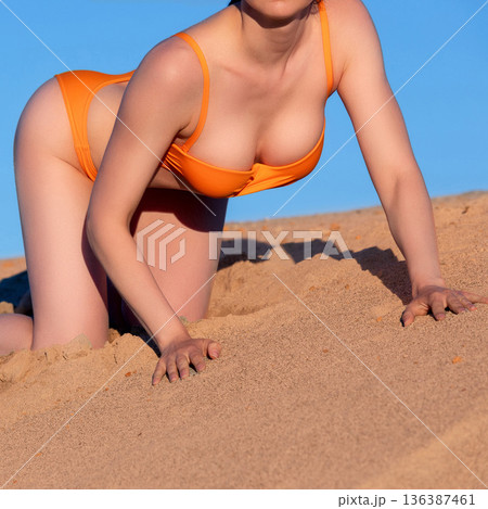 woman in orange swimsuit sitting on the sand on blue sky background woman in orange swimsuit sitting on the sand on blue sky background 136387461