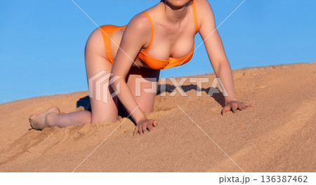 woman in orange swimsuit sitting on the sand on blue sky background 136387462