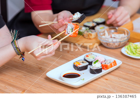Close up of female hands holding chopsticks and eating sushi rolls Close up of female hands holding chopsticks and eating sushi rolls 136387465