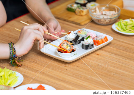 Close up of female hands holding chopsticks and eating sushi rolls. Close up of female hands holding chopsticks and eating sushi rolls. 136387466