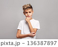 Stylish preteen blond boy posing as kid fashion model in studio portrait, isolated on grey background, looking confidently with dark brown eyes and modern beauty 136387897