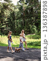 Happy family walking together with small dog along forest path on sunny day. Smiling mother with son and daughter enjoying outdoor lifestyle, slow living, quality time, summer leisure, full length 136387898